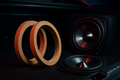 Create a realistic product shot of MDF speaker spacer rings next to car speakers or in a trunk installation. Show wood texture, clean edges, and metallic speaker cones, with a dark, moody JDM-inspired background and subtle red/blue lighting accents.