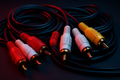RCA cables arranged neatly. Connectors visible, dark background, subtle red/blue neon reflections.